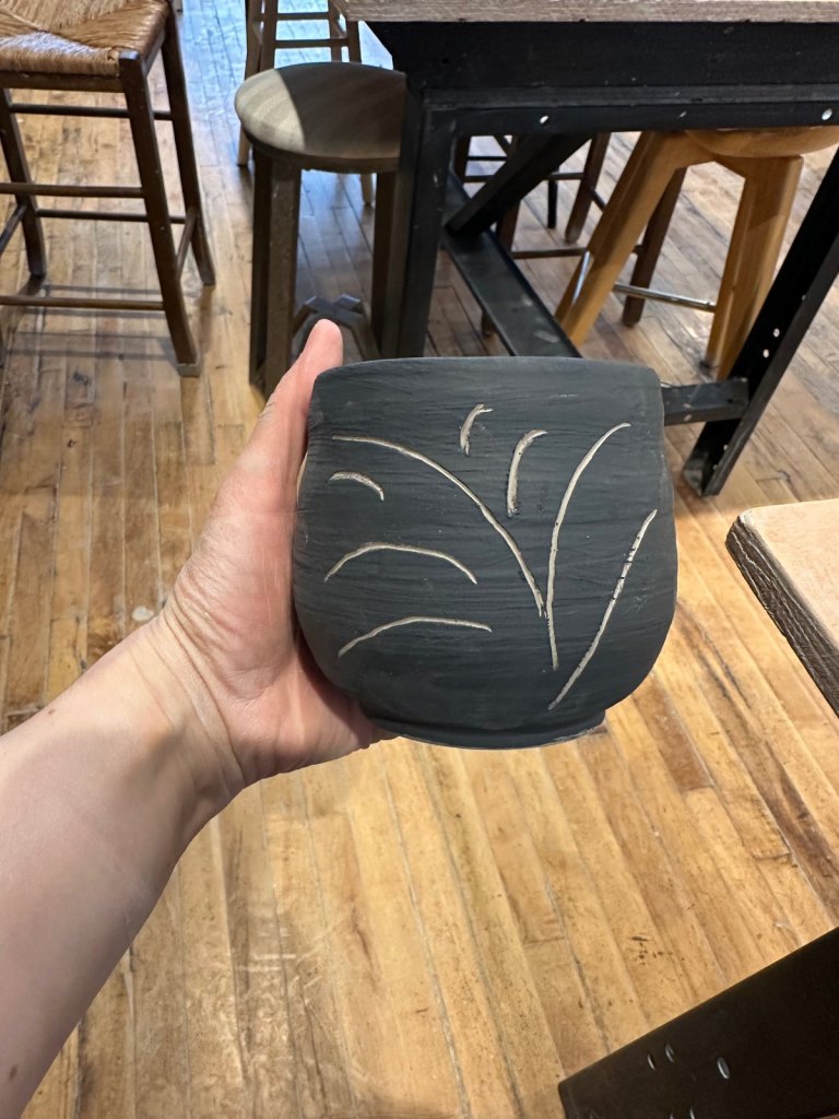 A small black pot with grasses carved through to the pale clay beneath