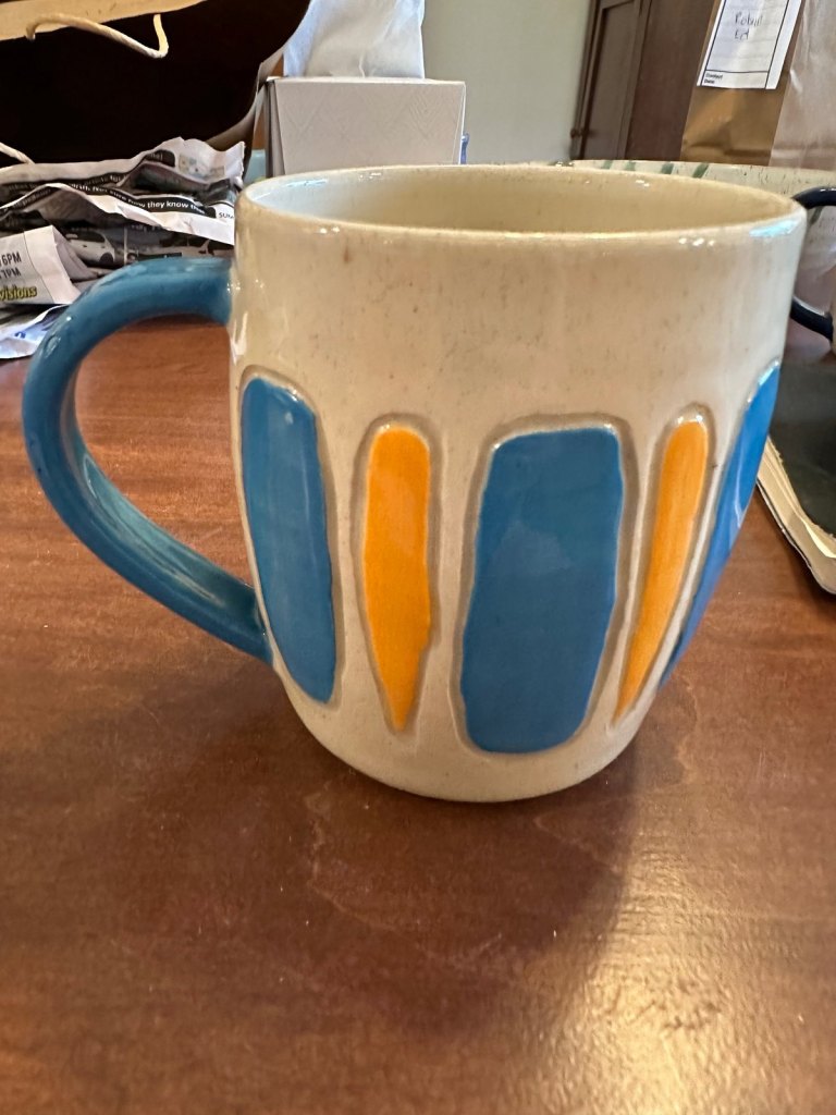 A cream speckled mug with inlaid bands of blue and yellow glaze and a blue handle