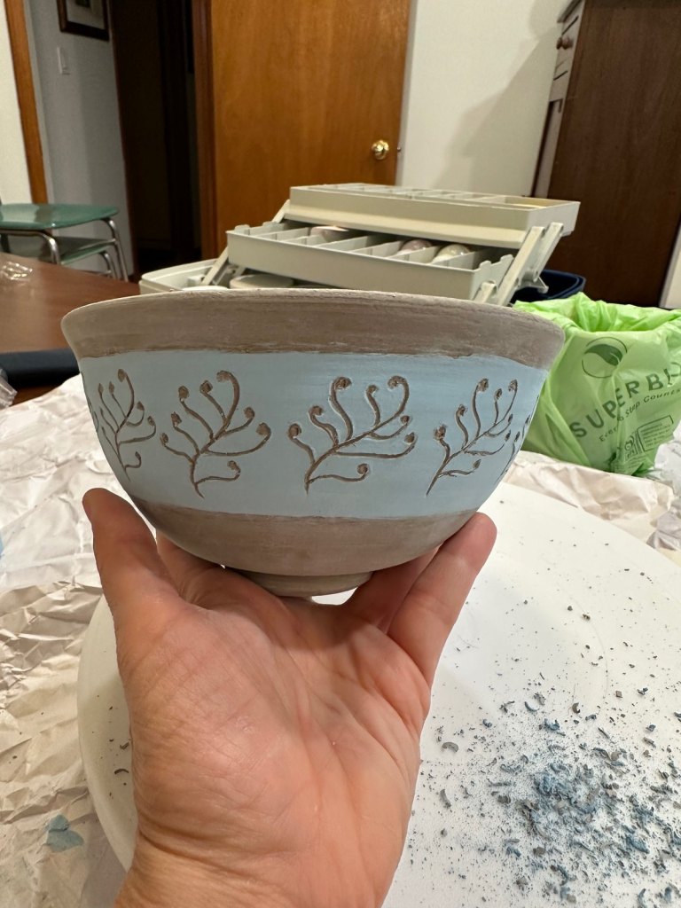 An unfired bowl with a pale blue band carved with curling sprigs