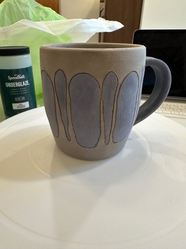 An unfired mug with outlined ovals painted in lavender-blue underglaze