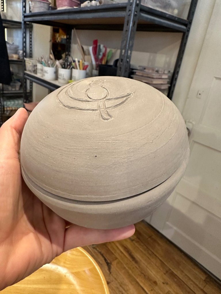 An unfired round urn with a cat on a crescent moon carved into the lid
