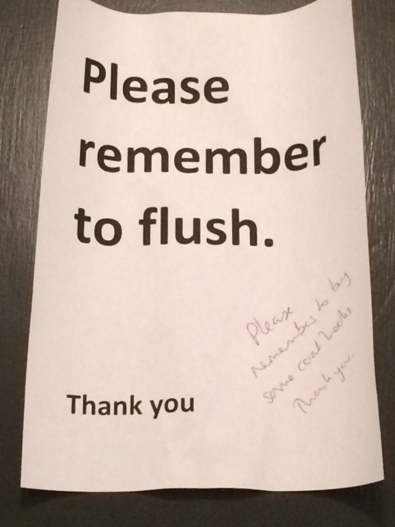 A printed sign reading Please remember to flush, with a handwritten addition: Please remember to buy some coat hooks. Thank you.