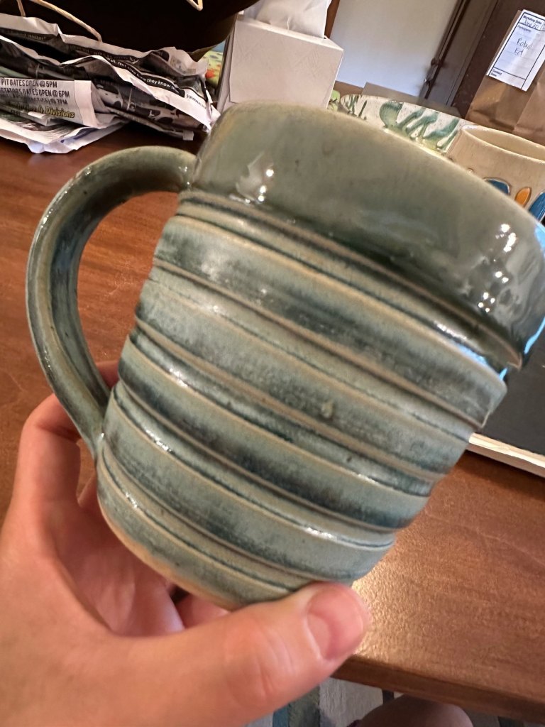 A wheel-thrown mug with carved horizontal ridges under a pale blue-green glaze
