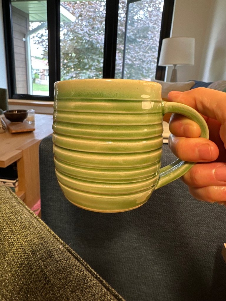 A ribbed mug in celadon glaze, held up in warm light